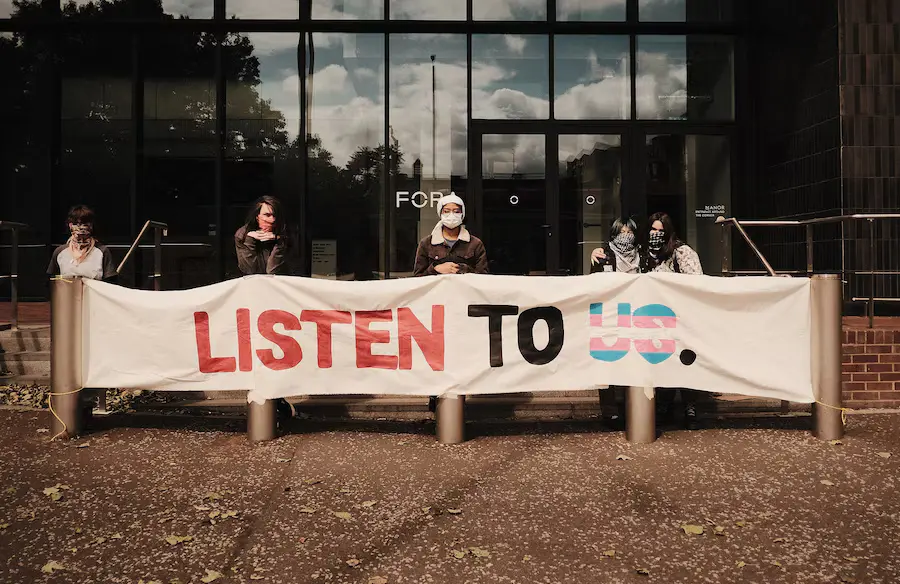 Photo of trans youth with banner "Listen to us"